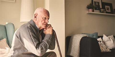 Elderly man sitting, leaning on cane in deep though.