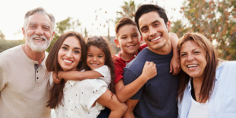 Three generation Hispanic family standing in the park, smiling to camera, selective focus