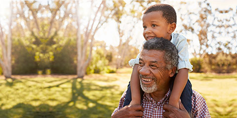 Black grandfather carries grandson on shoulders during walk in park