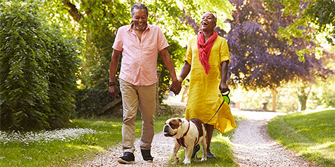 Older African-American couple walking down gravel path with a bulldog.