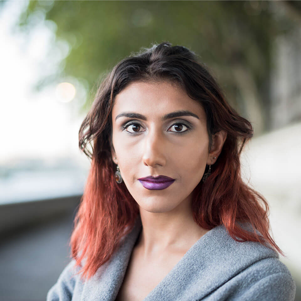 Portrait of contented transgender female, of middle eastern ethnicity with blurred park or riverwalk in background.