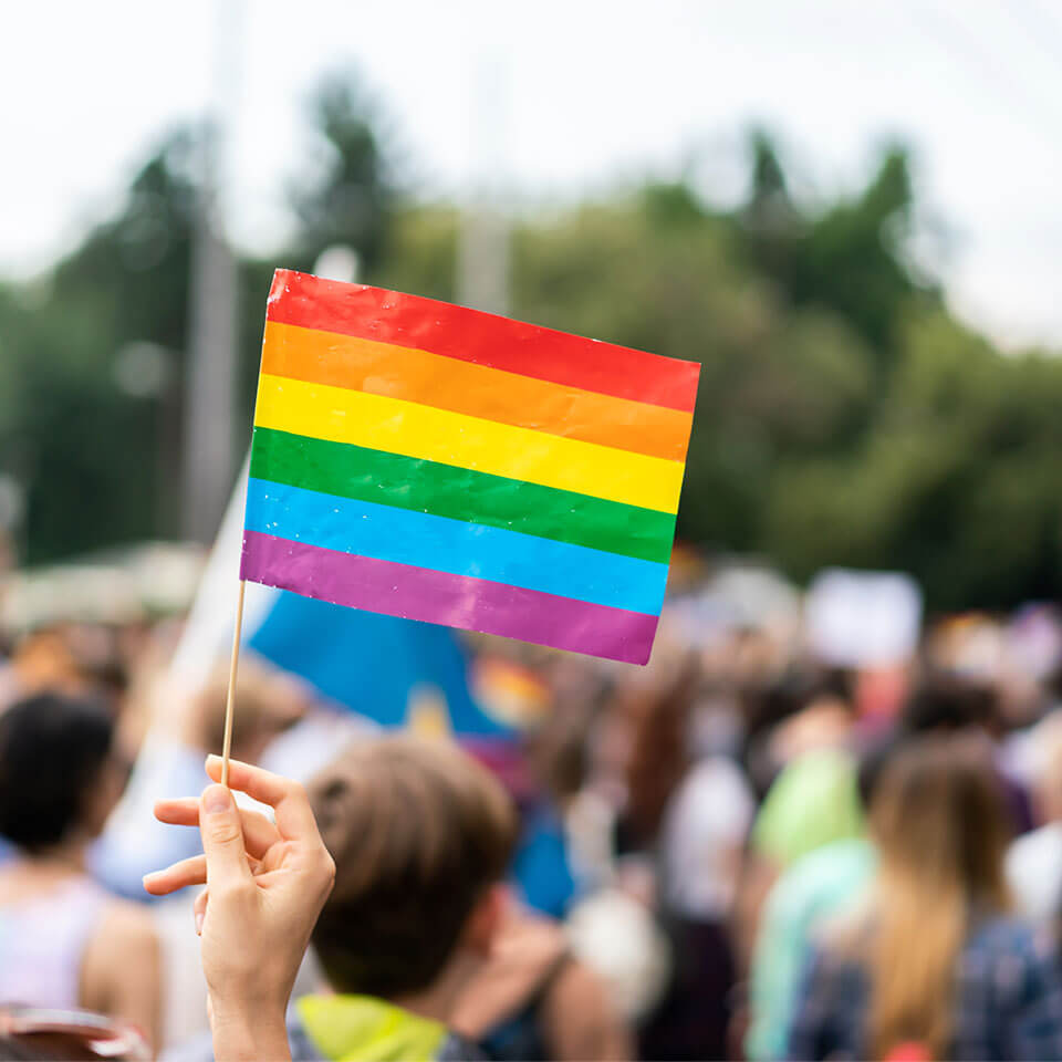 Rainbow flag at pride parade with blurred participants in the background