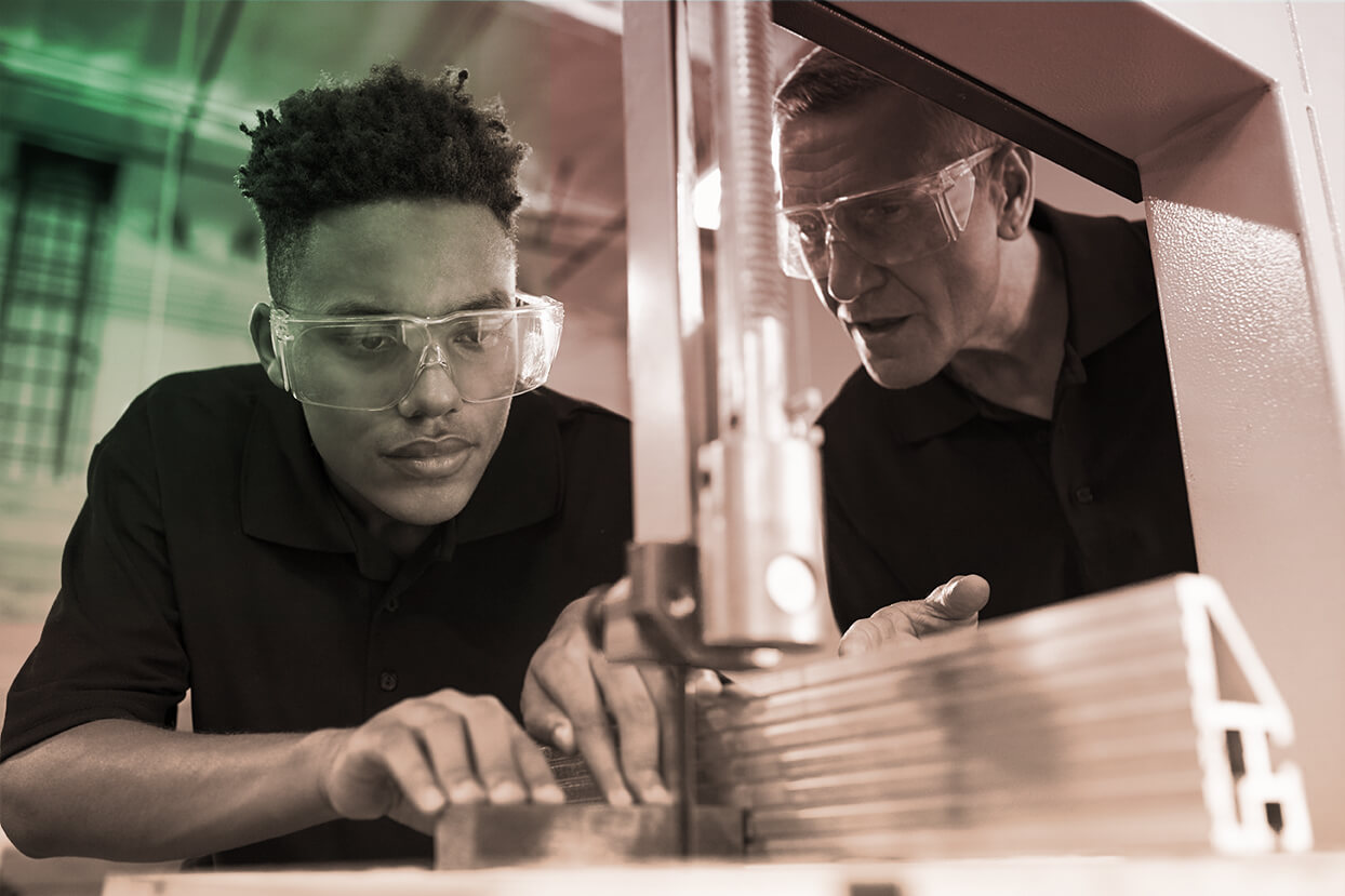 Photograph of older male instructing a younger male on how to use a machine.