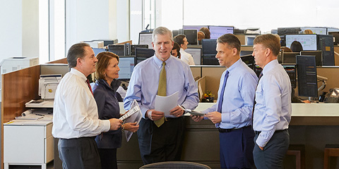 Photograph of Jay Schwister, Mary Ellen Stanek, Duane McAllister, Lyle Fitterer and Warren Pierson standing in semi-circle conversing in an office setting
